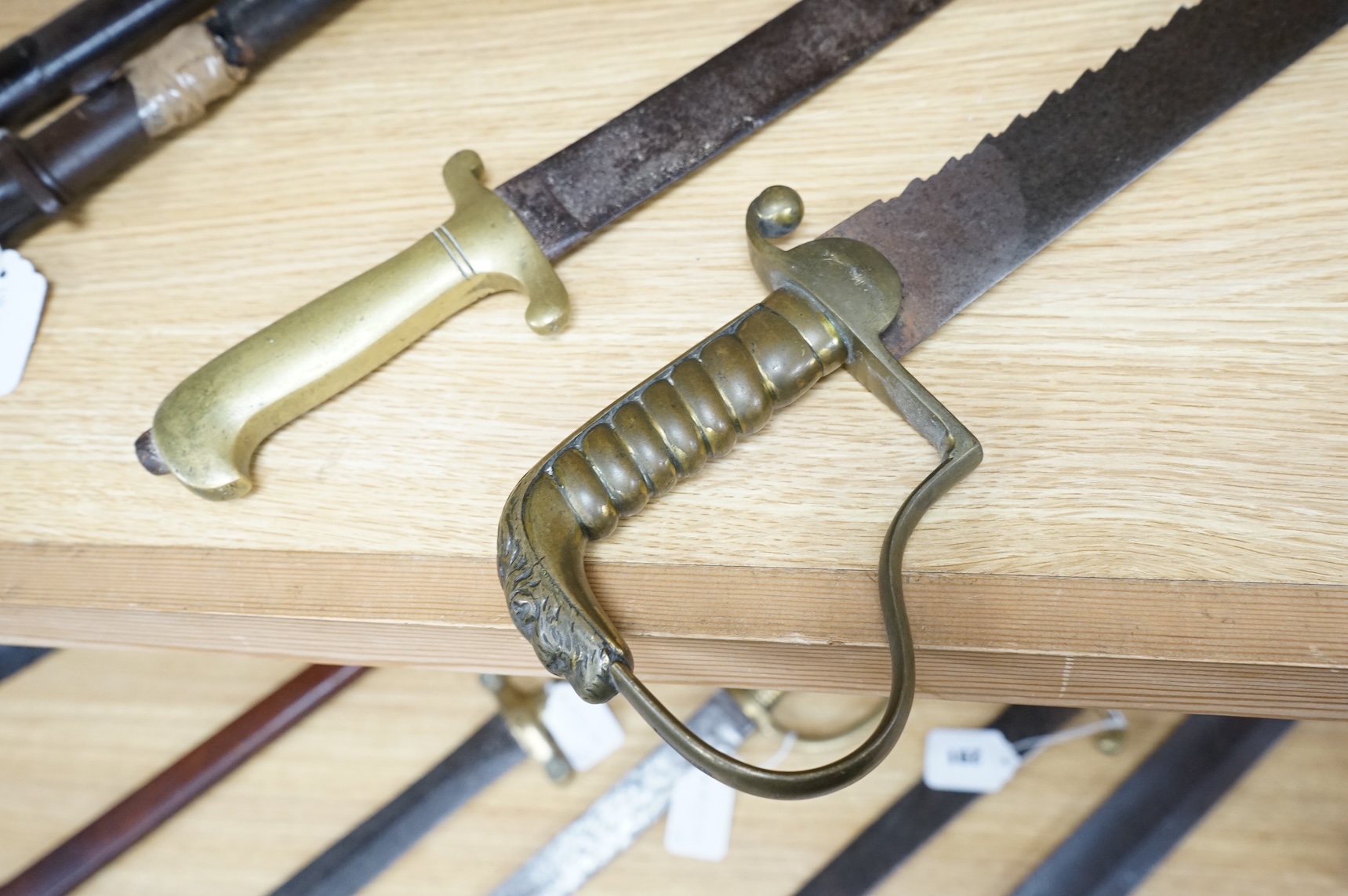 A British Pioneer’s sidearm with brass stirrup hilt, lion’s head pommel and sawback blade, together with an Imperial German sidearm with one piece brass hilt and slightly curved single edge blade